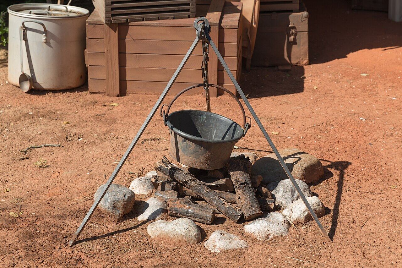 Cast-iron pot hanging from a tripod over a fire ring